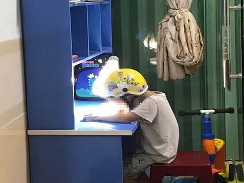 Sự thật đằng sau tấm ảnh học sinh lớp 1 phải đội mũ bảo hiểm ngồi làm bài tập khi bố mẹ đứng cạnh